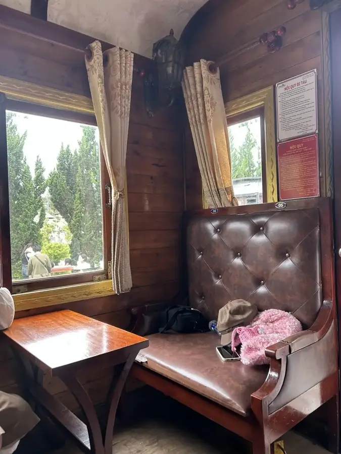 A compartment of the heritage train: a leather bench, a wooden table and a lantern — Trai Mat heritage train + pagoda, Da Lat